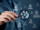 A person holds a magnifying glass focusing on icons of people, symbolizing analysis, recruitment, or searching for specific individuals within a group.