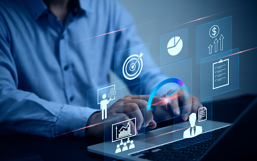 A person types on a laptop surrounded by digital business icons, including charts, graphs, a target, and a checklist, representing data analysis and business strategy.