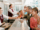 A family checks in at an airport counter for their group booking airline reservation, handing documents to a smiling employee while other travelers are assisted in the background.